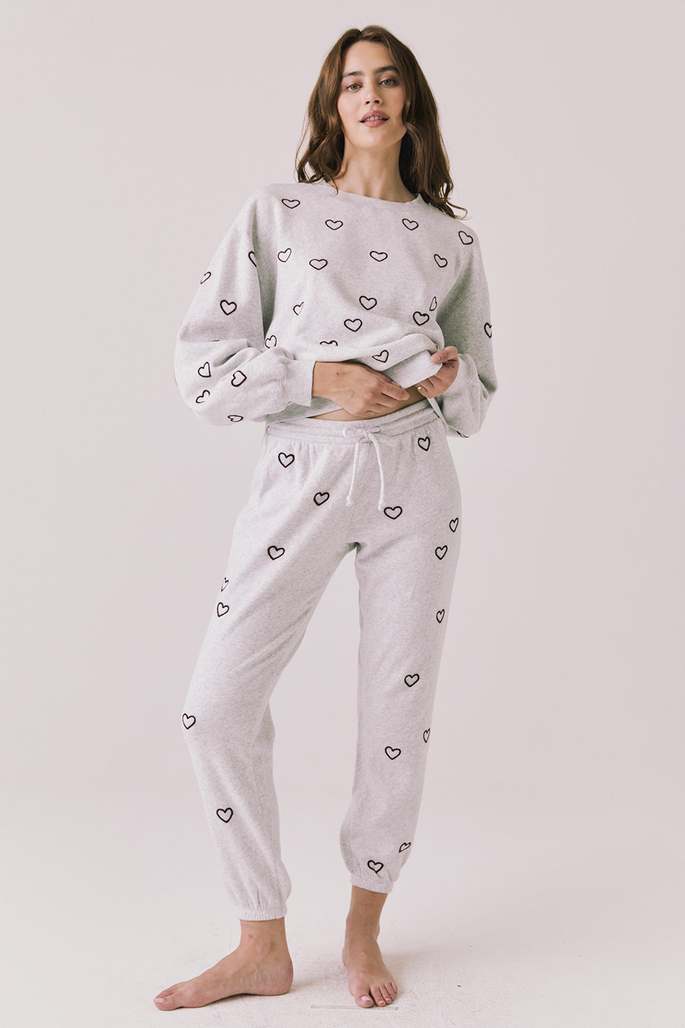Woman wearing a light gray pajama set with heart patterns .